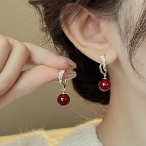 Detailed view of gold-tone geometric earrings with red beads and sparkling zircons