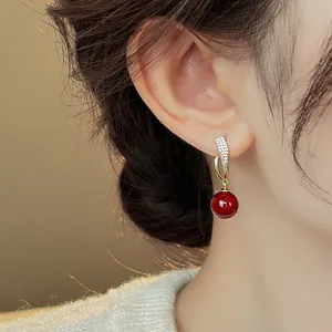 Close-up of elegant gold-toned earrings with zircon stones and a dangling red bead.