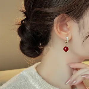 Close-up view of elegant gold zircon drop earrings with a red bead worn by a model