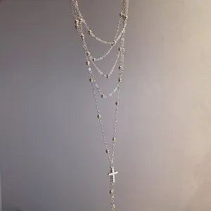 Detailed view of a layered silver necklace featuring a zircon-encrusted cross pendant.