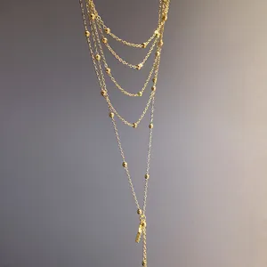 Detail view of layered gold chain necklace featuring delicate beads and a sleek pendant.