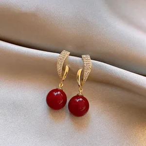 Detailed view of elegant irregular gold earrings with zircon stones and red beads