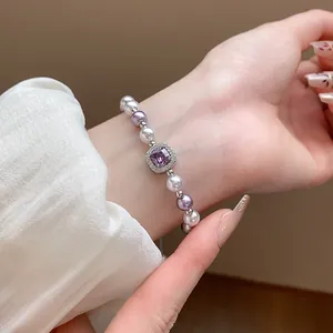 Elegant close-up of a French pearl bracelet with a purple square zircon centerpiece on wrist.