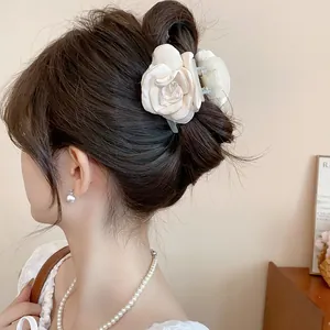 Elegant cream satin rose flower hair claw clip shown worn in a stylish messy bun hairstyle