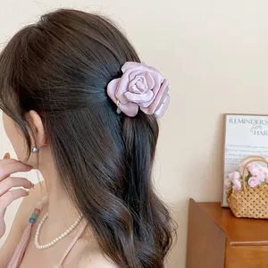 Detail view of a stylish pink satin fabric flower hair claw clip worn on wavy brown hair.