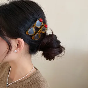 Detailed close-up showing yellow acrylic glasses-shaped hair clips with red apple accents