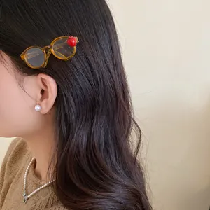Close-up of a unique acrylic hair clip shaped like glasses with a tiny red apple detail.