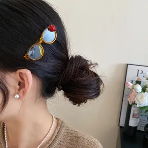 Close-up of a trendy amber acrylic hair clip shaped like glasses with a red apple charm.
