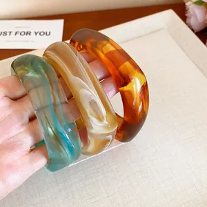 Detailed close-up of marbled resin bangles in green, beige, and amber brown tones