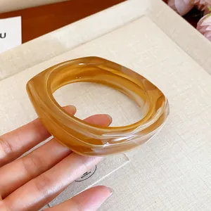 Amber marble square resin bangle held by hand, showing translucent swirl texture