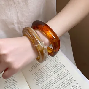 Detailed view of two marble-textured resin bangles in amber and cream tones