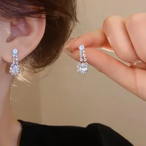 Detailed view of silver-toned water drop zircon stud earrings shown on model's ear and hand