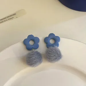 Detail view of cute blue flower stud earrings with grey fuzzy pom-poms on a plate
