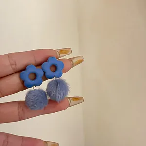 Blue flower earrings with purple pom-poms held in hand, minimalist jewelry detail view