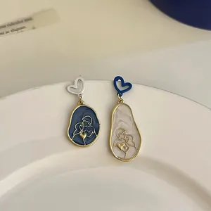 Detailed view of asymmetric heart and lover silhouette earrings on a minimalist white ceramic plate