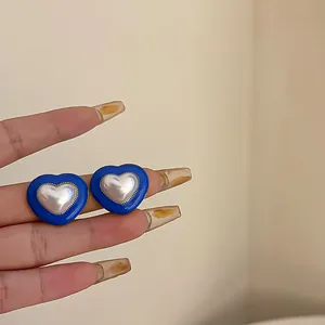 Detail of blue heart-shaped stud earrings with lustrous pearl centers and silver needles