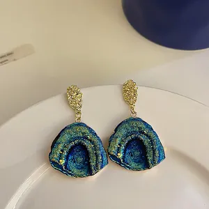 Detail of irregular geometric earrings with blue-green druzy crystal and gold-tone finish.