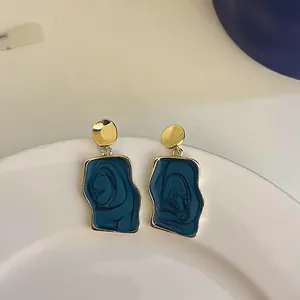 Close-up of irregular geometric earrings with deep blue marbled enamel and gold-tone finish