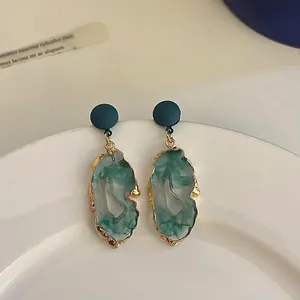 Detail shot of irregular green resin earrings with gold-tone edges on a white plate