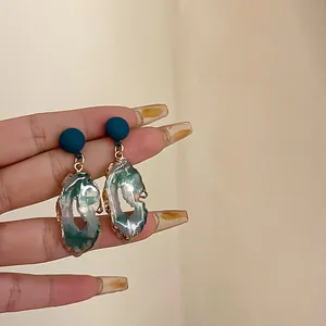 Detail of blue stud earrings with irregular green resin drops and gold trim