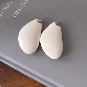 Primo piano di orecchini a goccia color crema minimalisti lucidi su un libro grigio