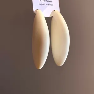 Dettaglio di eleganti orecchini a goccia color crema con finitura lucida per donne.