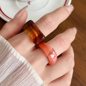 Close-up detail of marbled amber and coral acrylic geometric rings on finger