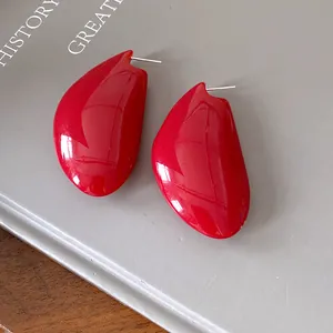 Primo piano di eleganti orecchini a goccia rosso vibrante su sfondo grigio minimalista
