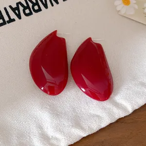 Primo piano di orecchini a lobo rosso scuro a forma di goccia su tela bianca.