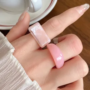 Close-up macro shot of pink marbled acrylic and smooth resin rings worn on a model's hand