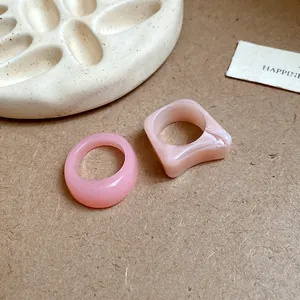 Macro view of pink acrylic marbled and solid geometric rings displayed on textured tray
