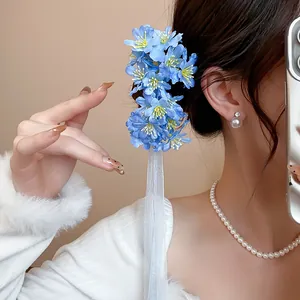 Primer plano de un pasador de pelo con flor de tela azul y borla de cinta blanca en modelo