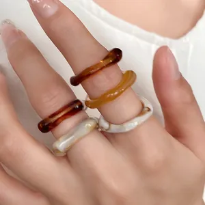 Close-up of stylish irregular acrylic rings with marbled and amber patterns on fingers
