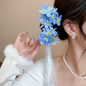 Primer plano de una horquilla de flores de tela azul con borlas de cinta blanca puesta.
