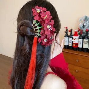 Vista detallada de un palillo para el pelo con flores de tela roja y borlas de cinta larga.