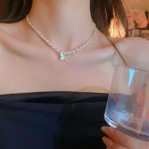 Close-up detail of a delicate butterfly pearl pendant necklace on a woman's collarbone.
