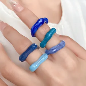 Detail of colorful irregular blue acrylic rings with marble swirl patterns on a hand.
