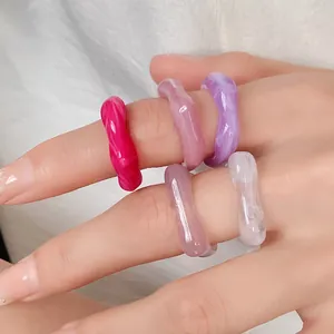 Detailed view of colorful acrylic irregular rings with marbled effects worn on hand.