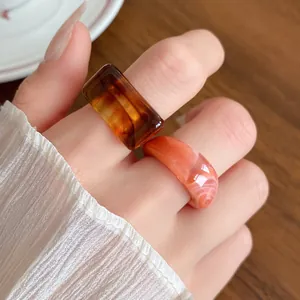 Detailed macro shot of stylish amber and coral marbled acrylic rings on woman's fingers