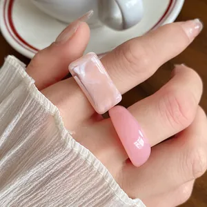 Close-up detail of pink marbled and solid acrylic geometric rings on a model's finger