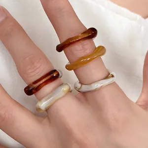 Close-up view of marbled acrylic rings featuring irregular wavy geometric shapes on hand