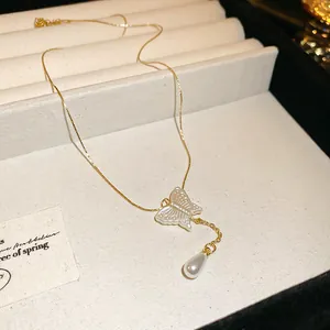 Macro detail of a delicate golden butterfly and white teardrop pearl pendant necklace