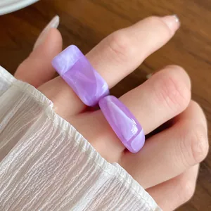 Close-up of purple marbled acrylic geometric rings on finger with white sleeve detail.