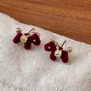 Close-up of elegant gold-toned horse stud earrings with deep red flocked texture.