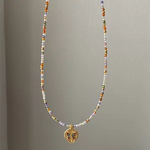 Detailed macro shot of a dainty colorful beaded necklace with a gold butterfly pendant