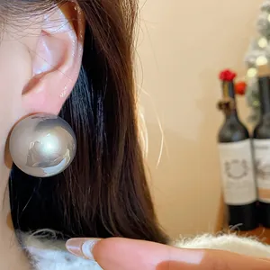 Primo piano di un grande orecchino a bottone sferico metallico argento minimalista su un orecchio