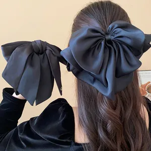 Close-up detail of an oversized black satin bow hair clip styled on model's wavy hair