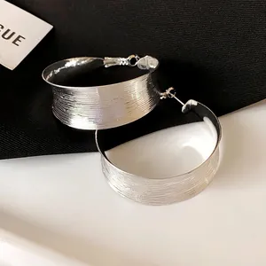 Primo piano di grandi orecchini a cerchio argento con texture spazzolata e design geometrico