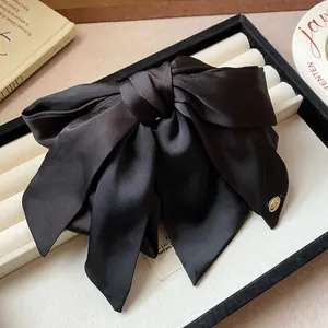 Detailed view of the elegant large black satin bow hair claw clip with a gold metal charm.