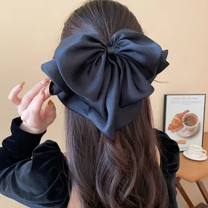 Detailed view of a large black satin bow hair claw clip styled on long wavy hair.